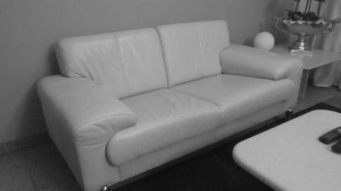 Ein weißes Glattledersofa steht in einem modernen Wohnzimmer und wirkt sauber und gepflegt in der stilvollen Umgebung.