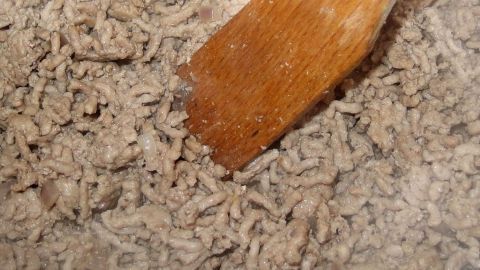 Hackfleisch wird mit einem Holzlöffel in einer Pfanne angebraten, um wässriges Hackfleisch beim Kochen zu vermeiden.