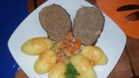 Auf einem Teller liegen zwei Scheiben Falscher Hase (Hackbraten) umgeben von gekochten Kartoffeln und Gemüse.