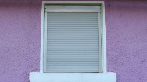 Ein Rollladen schließt ein Fenster in einer lila Wand, um Heizkosten zu sparen, indem er Wärme im Raum hält.