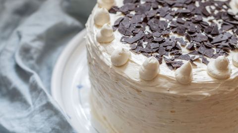 Eine Torte mit einer cremigen Schicht und Schokoladenspänen liegt auf einem weißen Teller, umgeben von einem sanften, grauen Tuch.