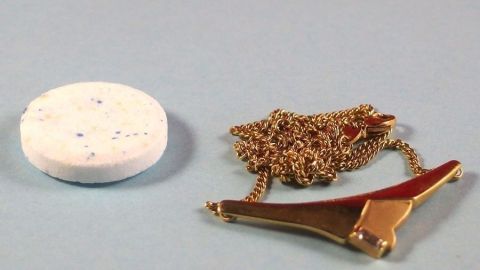 Einfach Gebissreiniger auflösen und den Schmuck für mehrere Stunden darin liegen lassen. Eventuell mit einem Brillenputztuch nachpolieren. Ein Schmuckstück liegt neben einem Gebissreiniger. Der Reiniger steht bereit, um den Schmuck zu säubern und aufzufrischen.