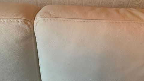 Eine helle Kunstledercouch zeigt Farbflecken an den Kanten, die möglicherweise mit Nagellackentferner behandelt werden sollen.