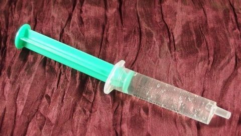 Eine Spritze mit grünem Griff liegt auf einem rot strukturierten Untergrund, bereit für die Nasendusche bei Schnupfen.