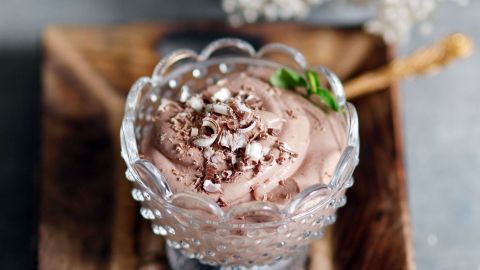 Eine zarte Mousse au Chocolat in einem eleganten Glas, garniert mit Schokoladenspänen, steht auf einem rustikalen Holzbrett.