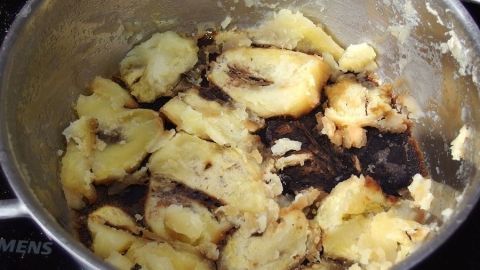 Ein stark angebrannter Topf enthält verkohlte Stücke von einem Gericht, das beim Kochen in einer Küche misslungen ist.
