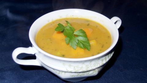 Eine cremige Kartoffelcremesuppe befindet sich in einer weißen Schüssel, dekoriert mit frischem Grün, auf einem dunklen Tisch.