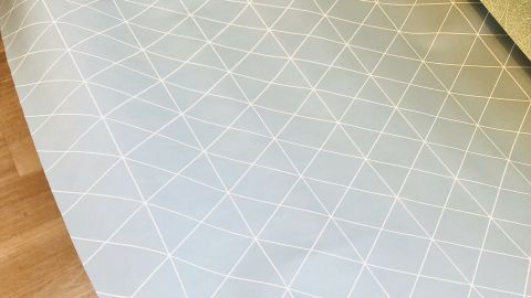 Ein handgehaltenes Wachstuch mit einem geometrischen Muster wird bereitgelegt, um eine Küchenausstattung ansprechend zu gestalten.