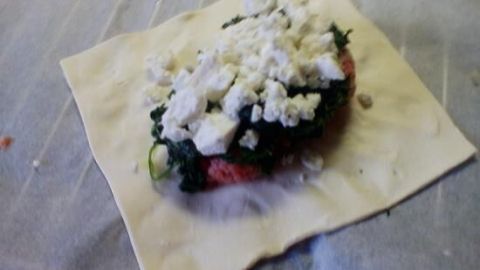 Eine Blätterteigtasche liegt auf einer Fläche, gefüllt mit einer Mischung aus Spinat und Feta. Das Umfeld ist hell und neutral.