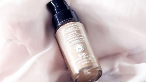 Ein Make-up-Fläschchen liegt auf einem weichen, rosafarbenen Stoff. Es zeigt, wie Make-up auf Textilien landet.