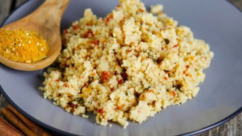Couscous liegt auf einem Teller und wird mit einer Gewürzmischung und einem Holzlöffel serviert, umgeben von Zimtstangen.