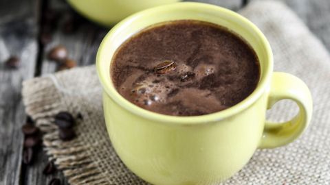 Zwei gelbe Tassen mit Dänischem Kaffelikör stehen auf einem rustikalen Holztisch, umgeben von Kaffeebohnen.