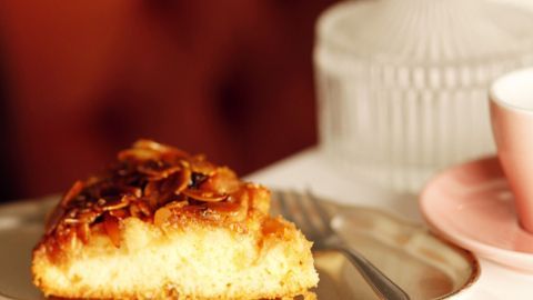 Ein Stück Florentiner Apfelkuchen liegt auf einem silbernen Teller, umgeben von einer eleganten Kaffeetasse und einer Glasglocke.