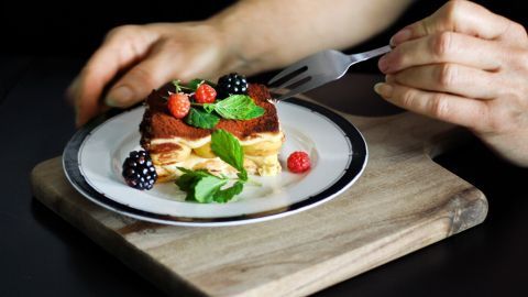Ein Stück kalorienarmes Tiramisu wird auf einem Teller mit frischen Beeren und Minze genossen, bereit zum Essen.