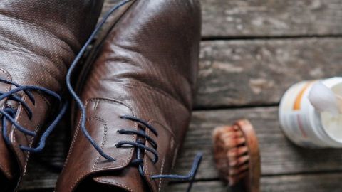 Schuhcreme kann ziemlich teuer sein. Putze deine Schuhe doch stattdessen mit Melkfett! Du wirst über den Effekt erstaunt sein. Braune Schuhe liegen auf einem Holzfußboden, während eine Bürste und Melkfett daneben bereitstehen, um die Schuhe zu pflegen.