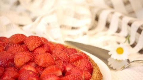 Erdbeerkuchen mit dichten, saftigen Früchten liegt auf einem Teller; im Hintergrund ein dekoratives Tuch und eine Blume.