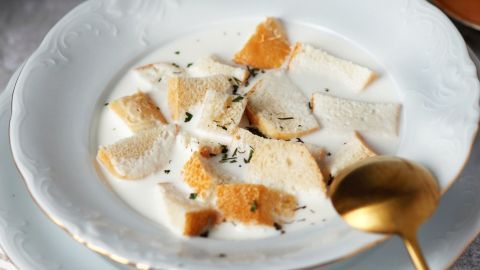Genieße eine köstliche Weckensuppe mit Milch, die aus alten Brötchen zubereitet wird. Diese einfache, aber schmackhafte Suppe ist eine ideale Möglichkeit, Reste zu verwerten und dabei den vollen Geschmack zu erleben. Eine weiße Schüssel enthält Weckensuppe mit Milch und alten Brötchen, garniert mit etwas Kräutern, auf einem Tisch.