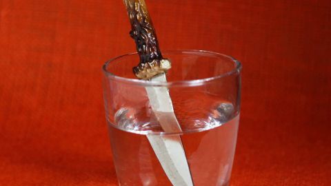 Ein Glas Wasser steht auf einem roten Hintergrund, während ein Messer mit einem besonderen Griff darin steckt.