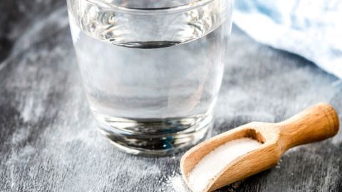 Ein Glas Salzwasser steht auf einer Arbeitsfläche, daneben liegt ein Holzlöffel mit Salz, um Übelkeit zu lindern.