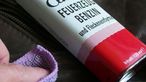 Eine Hand hält ein Tuch, während sie Feinbenzin von einer roten Dose abgibt, um damit ein Feuerzeug zu befüllen.