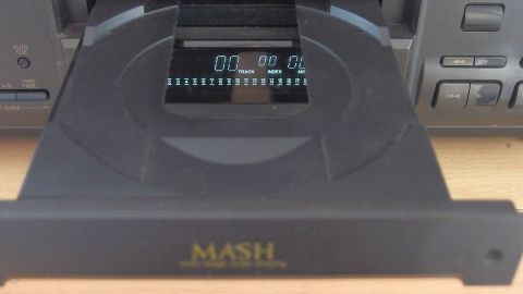 CD-Laufwerk öffnet sich, zeigt Display mit "TRACK" und "INDEX" in einem Hifi-Gerätumfeld. Text: "MASH".