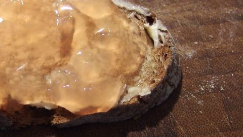 Ein Stück Brot liegt auf einer Oberfläche, bestrichen mit glänzender Quittenmarmelade in einem rustikalen Umfeld.