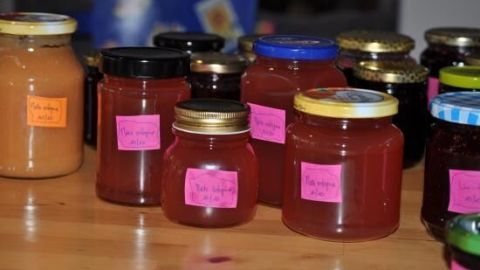 Gläser mit bunten Etiketten stehen auf einem Tisch, die Milchprodukte wie Marmelade oder Säfte enthalten.