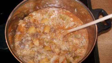 Ein Topf Wirsingeintopf köchelt auf dem Herd, gefüllt mit Wirsing, Kartoffeln und Fleisch, umgerührt mit einem Holzlöffel.