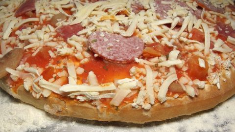 Eine Pizza mit Käse und Salami liegt auf einer bemehlten Fläche, bereit für das Backen, um knusprig zu werden.