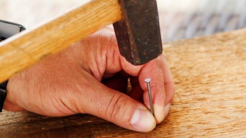 Holz spaltet nicht, wenn man vor dem Einschlagen eines Nagels dem Nagel die Spitze entfernt (feilen oder abkneifen mit einer Kombizange).. Ein Hammer schlägt Nägel ohne Splittern in ein Holzstück, während eine Hand das Nagelende sicher hält.