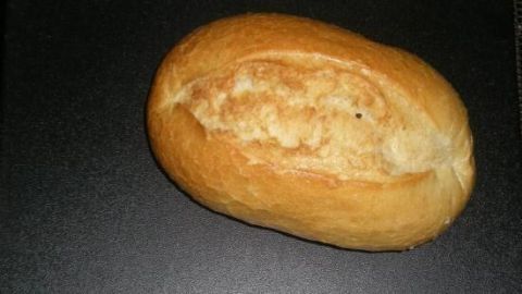 Ein Brötchen liegt auf einer dunklen Oberfläche und wartet darauf, im Ofen aufgebacken zu werden, um frisch und knusprig zu sein.