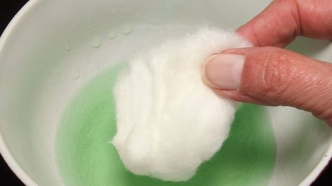 Eine Hand hält ein Wattepad, das in grünem Fensterspray getränkt ist, bereit zur Reinigung einer engen Vase.