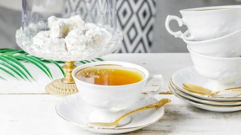 Eine elegante Teetasse mit Mate-Tee steht neben einer gläsernen Kuppel mit Süßigkeiten auf einem weißen Tisch.