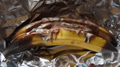 Eine Schokobanane aus dem Ofen liegt in Alufolie, während die Schokolade über die Banane schmilzt und sich vermischt.