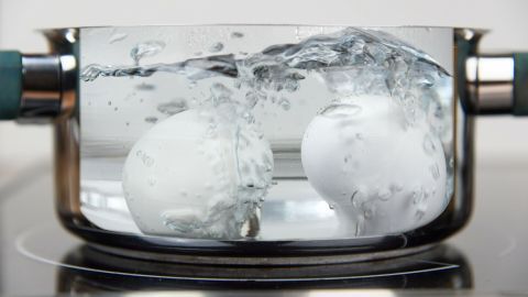 Zwei Eier spritzen in einem Topf mit kochendem Wasser auf einem Herd. Die Luft ist dampfig und heiß.