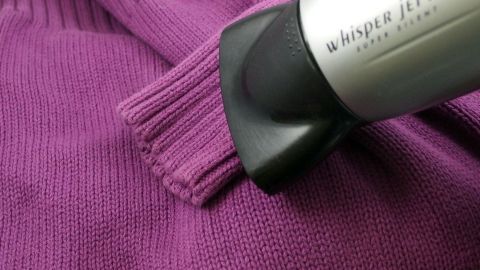 Um die Bündchen von Wollpullovern zu frischt und in Form zu halten, kann eine spezielle Technik mit einem Fön angewendet werden. Diese Methode hilft, das Ausleiern zu verhindern und sorgt für eine lange Lebensdauer deines Pullovers. Ein Wollpullover in lila wird mit einem elektrischen Gerät bearbeitet, um die Bündchen zu straffen und zu reinigen.