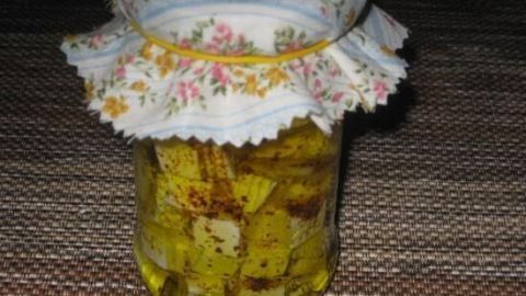 Ein Glas mit eingelegtem Schafskäse oder Feta schwimmt in einer aromatischen Öl-Lösung, mit Blümchenmuster-Deckel.