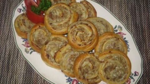 Leckere Hackschnecken aus Blätterteig liegen auf einem dekorativen Teller, umgeben von frischen Tomaten und Petersilie.