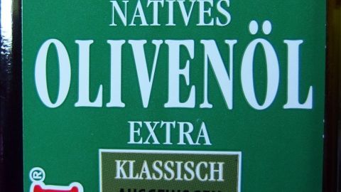 Eine Flasche natives Olivenöl steht im Vordergrund, beschriftet mit „Klassisch Ausgewogen“, umgeben von einer neutralen Umgebung.
