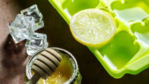 Eiswürfel aus einer grünen Form stehen neben Honig und einer Zitronenscheibe auf einem Tisch, ideal bei Halsschmerzen.