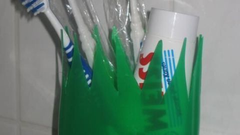 Eine grüne, flaschenförmige Halterung steht im Badezimmer und hält Zahnbürsten sowie eine Zahnpasta.