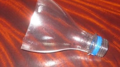 Ein selbst hergestellter Trichter aus einer Plastikflasche liegt auf einem Holzuntergrund und spiegelt das Licht.