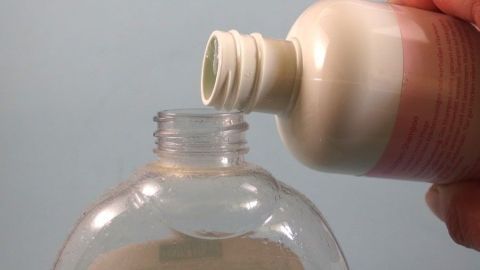 Eine Hand gießt Shampoo in einen leeren Flüssigseifen-Behälter, bevor er für die Dusche verwendet wird.