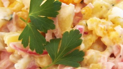 Ein Kartoffelsalat wird appetitlich präsentiert, garniert mit frischen Petersilienblättern und umgeben von einem hellen Hintergrund.