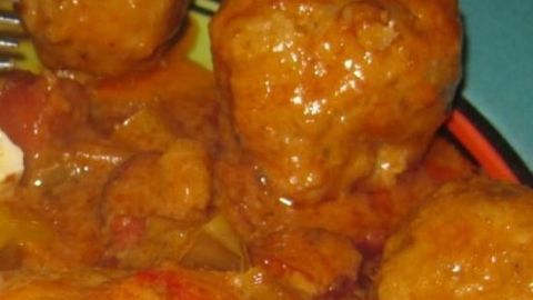 Scharfe B&auml;llchen in einer w&uuml;rzigen Sauce liegen auf einem bunten Teller, umgeben von frischem Gem&uuml;se.