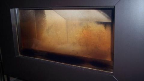 Die Kaminscheibe ist verschmutzt mit Asche und Rauch, was auf einen regelmäßigen Gebrauch des Kamins hinweist.