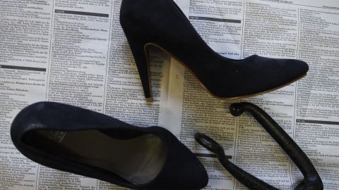 Schwarze High Heels liegen auf einer Zeitung, während ein Schuhdehner daneben zur Weitung drückender Schuhe bereitsteht.