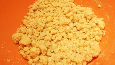 Eine handgroße Menge Streusel liegt in einer orangenen Schüssel, bereit zum Backen von Mandel- oder Nuss-Streuseln.