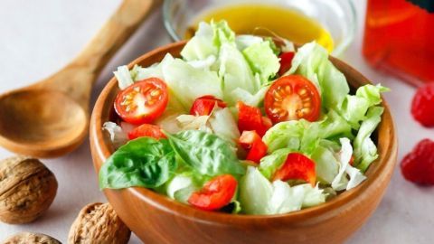 Frischer Salat mit Tomaten in einer Schüssel, umgeben von Walnüssen und einem Glas Himbeeressig.