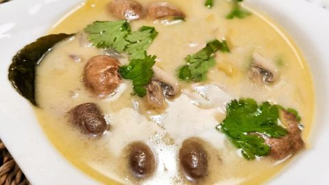 Eine cremige Champignon-Cremesuppe mit frischen Kräutern in einer weißen Schüssel auf einem rustikalen Tisch.